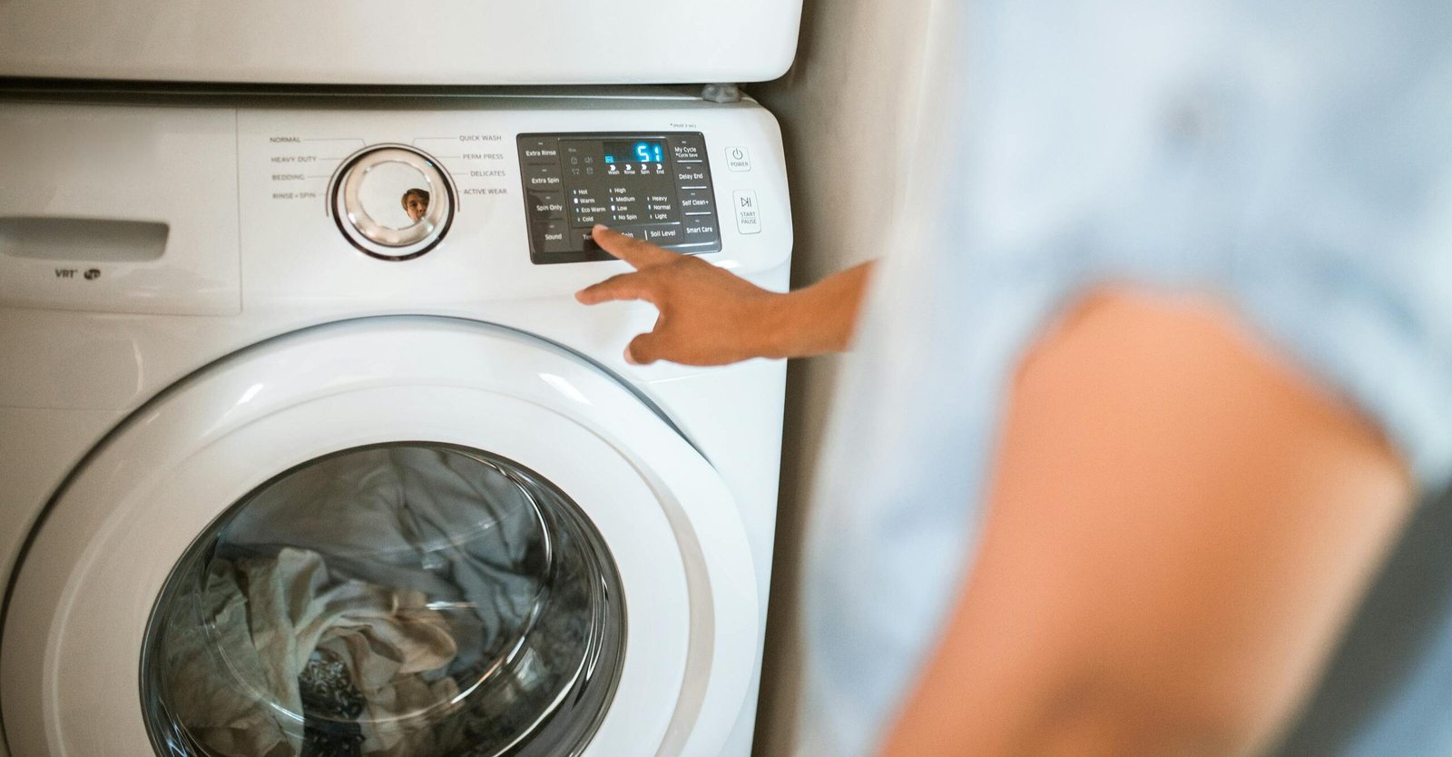 Hand selecting laundry options on a digital washing machine control panel indoors.